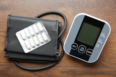 Photo of Blood pressure measuring device and pills on wooden table, top view