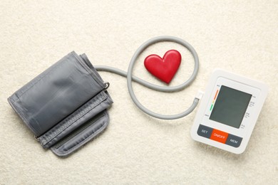 Photo of Blood pressure measuring device and heart figure on light textured background, top view