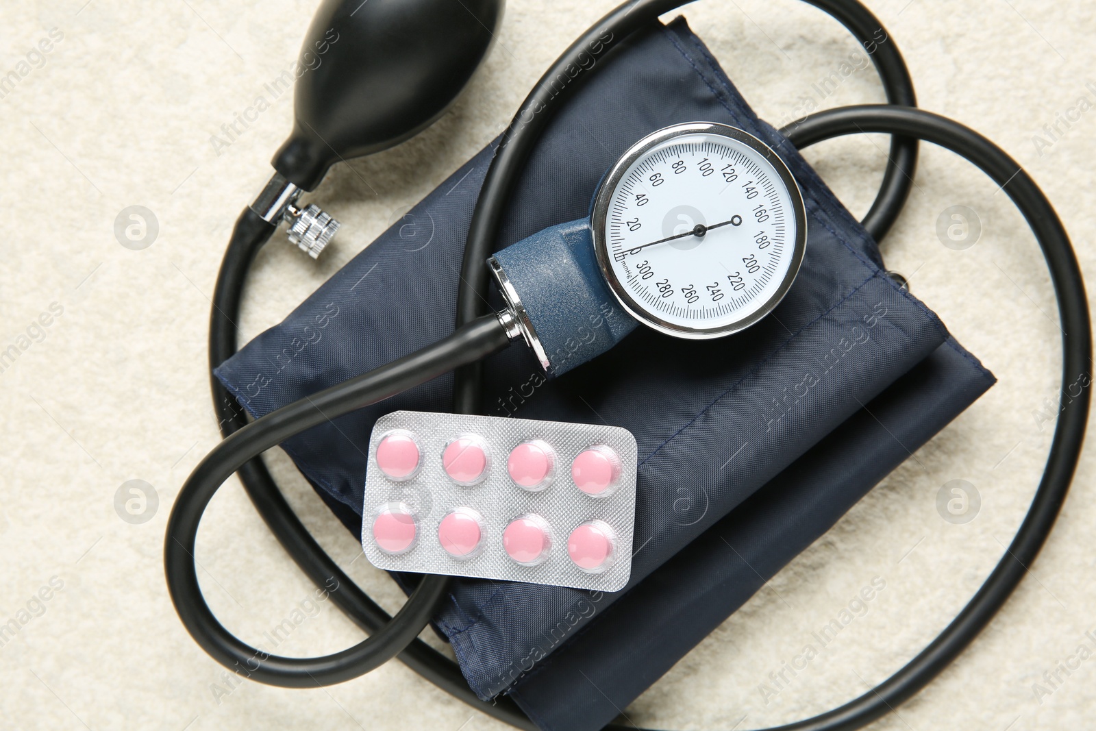 Photo of Blood pressure measuring device and pills on light textured background, top view