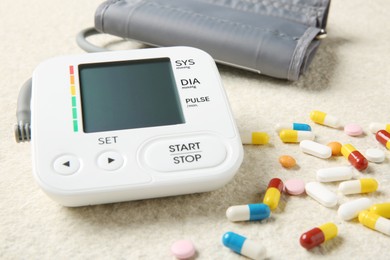 Photo of Blood pressure measuring device and pills on light textured background, closeup