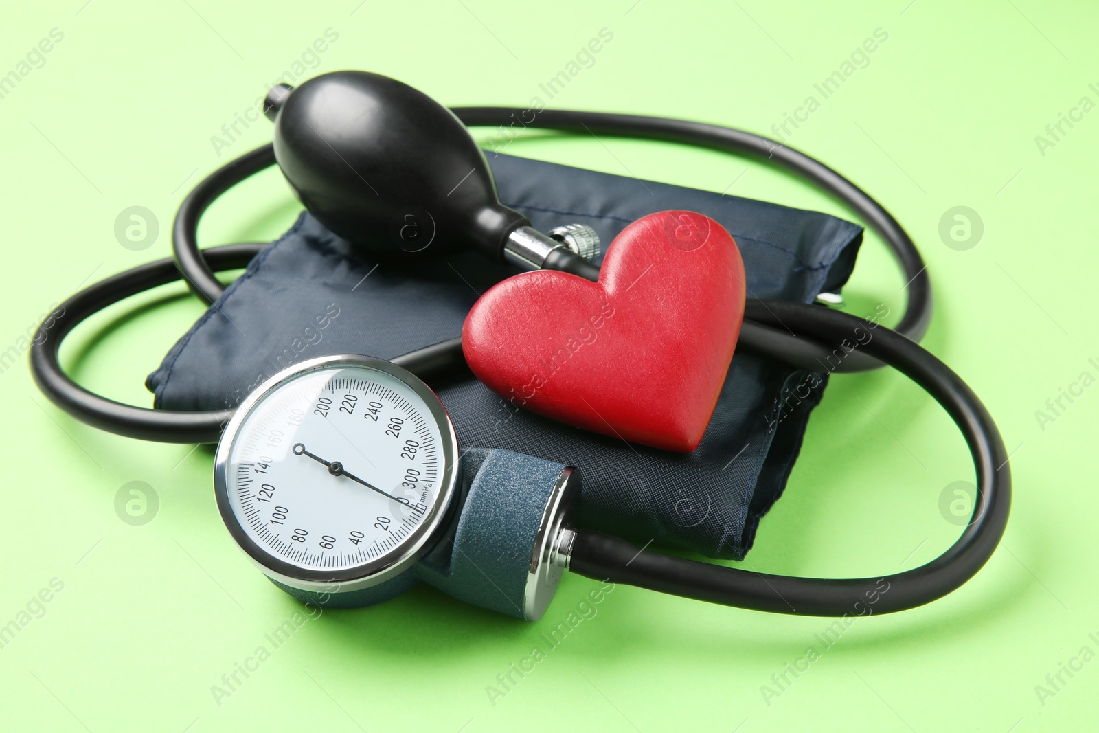 Photo of Blood pressure measuring device and heart figure on green background, closeup