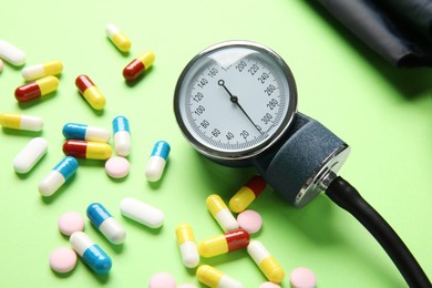 Photo of Blood pressure measuring device and pills on green background, closeup