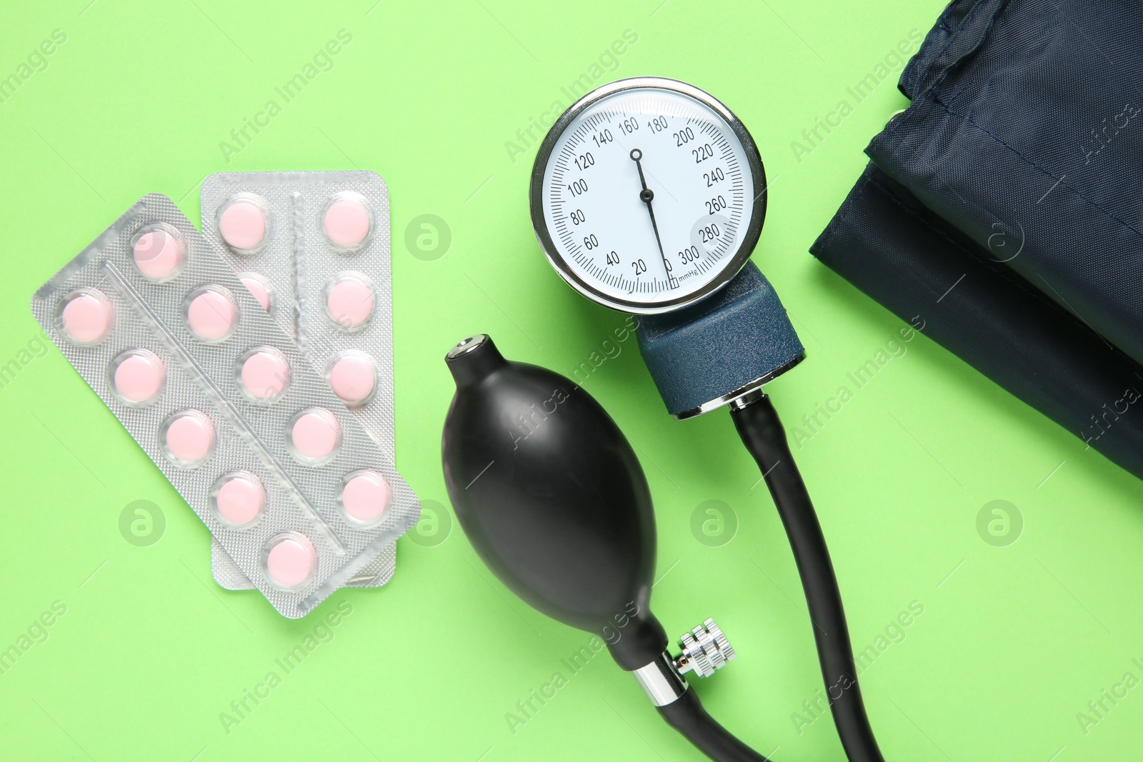 Photo of Blood pressure measuring device and pills on green background, top view