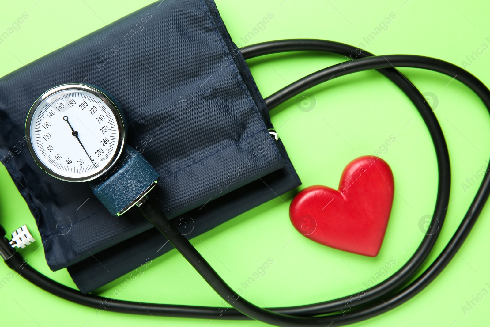 Photo of Blood pressure measuring device and heart figure on green background, top view