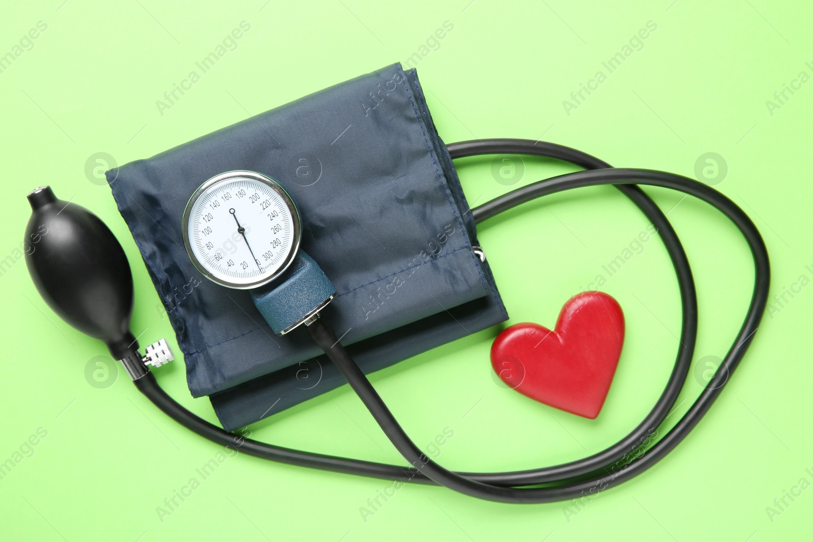 Photo of Blood pressure measuring device and heart figure on green background, top view