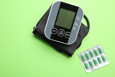 Photo of Blood pressure measuring device and pills on green background, top view