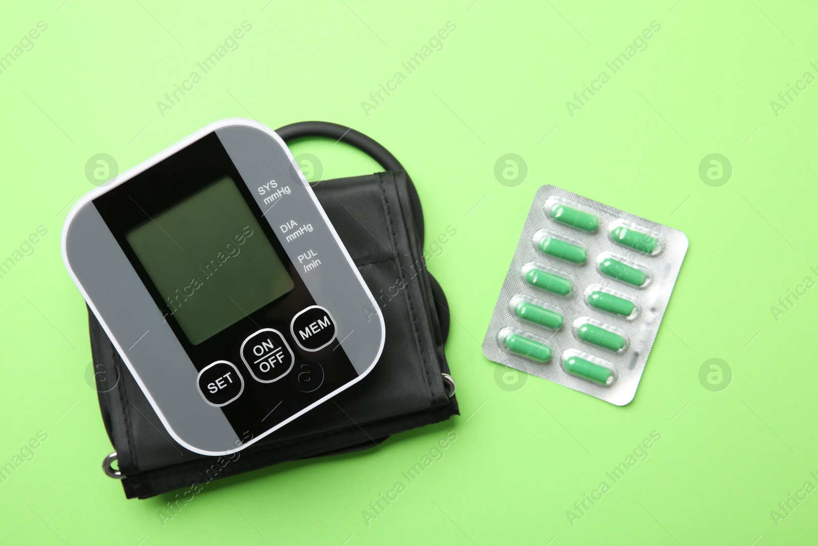 Photo of Blood pressure measuring device and pills on green background, top view