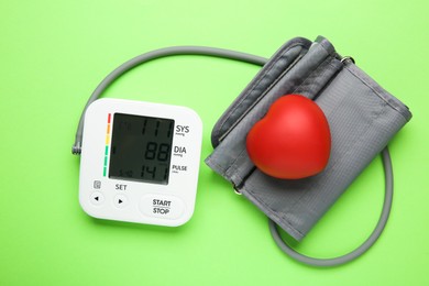 Photo of Blood pressure measuring device and squeeze heart on green background, top view