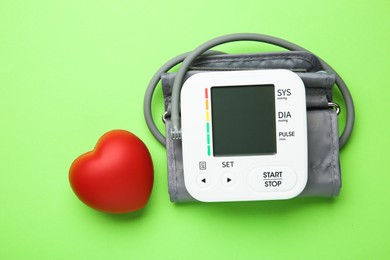 Photo of Blood pressure measuring device and squeeze heart on green background, top view