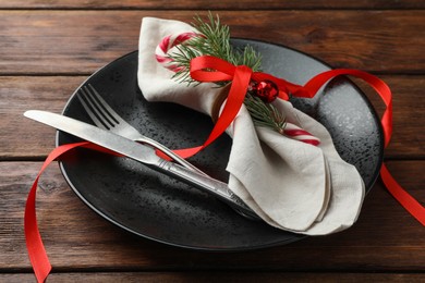 Photo of Christmas setting with plate, cutlery, fir branches and ribbon on wooden table, closeup