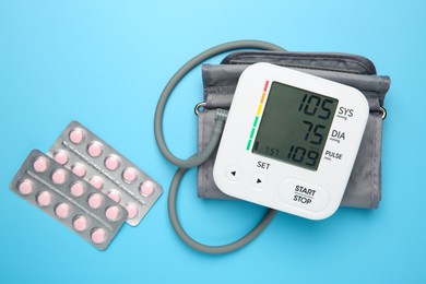 Photo of Blood pressure measuring device and pill blisters on light blue background, flat lay