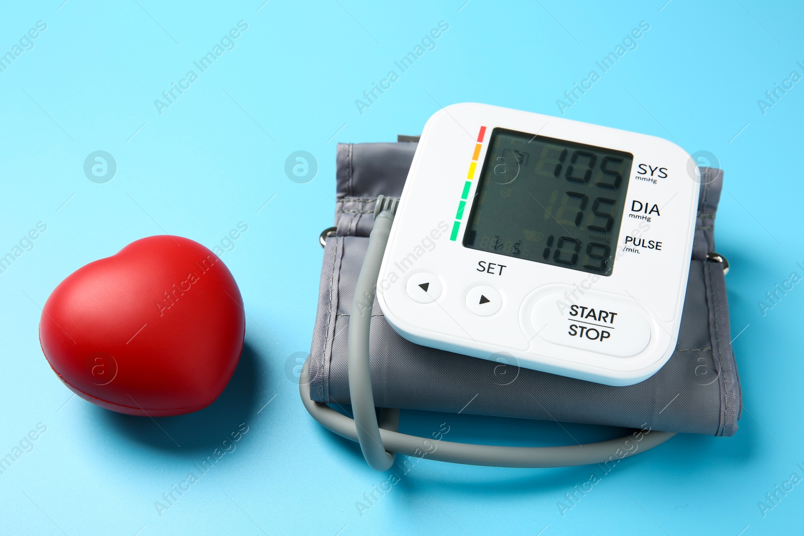 Photo of Blood pressure measuring device and red heart figure on light blue background