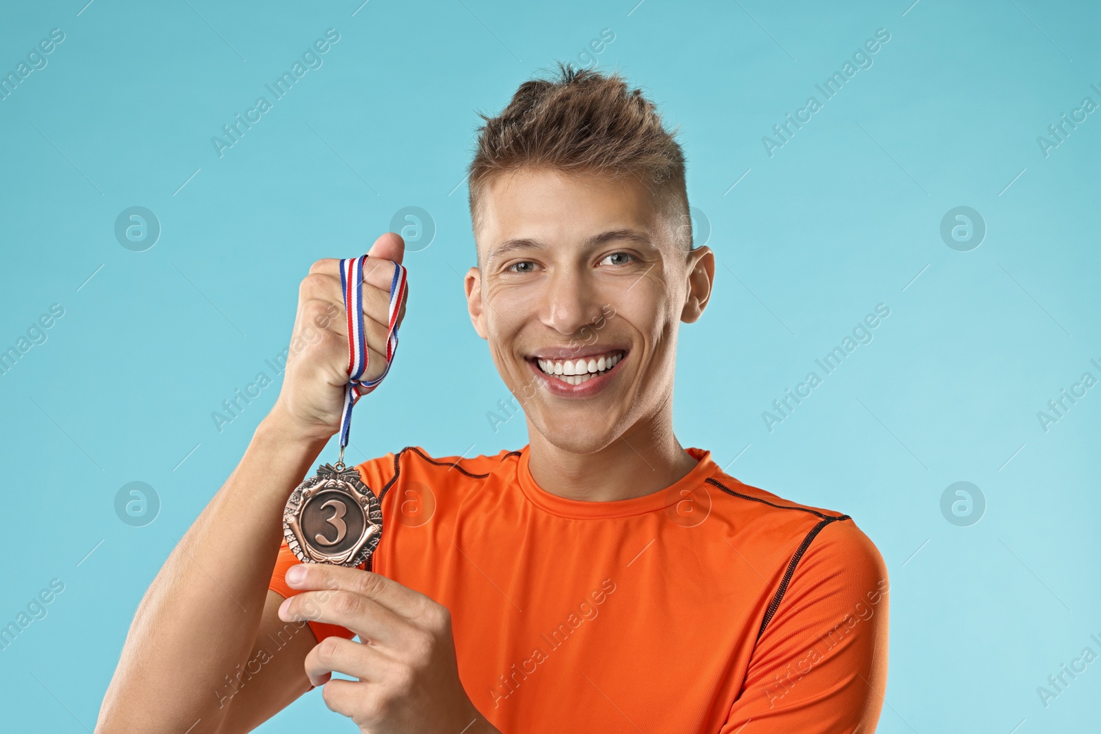 Photo of Happy winner with bronze medal on light blue background