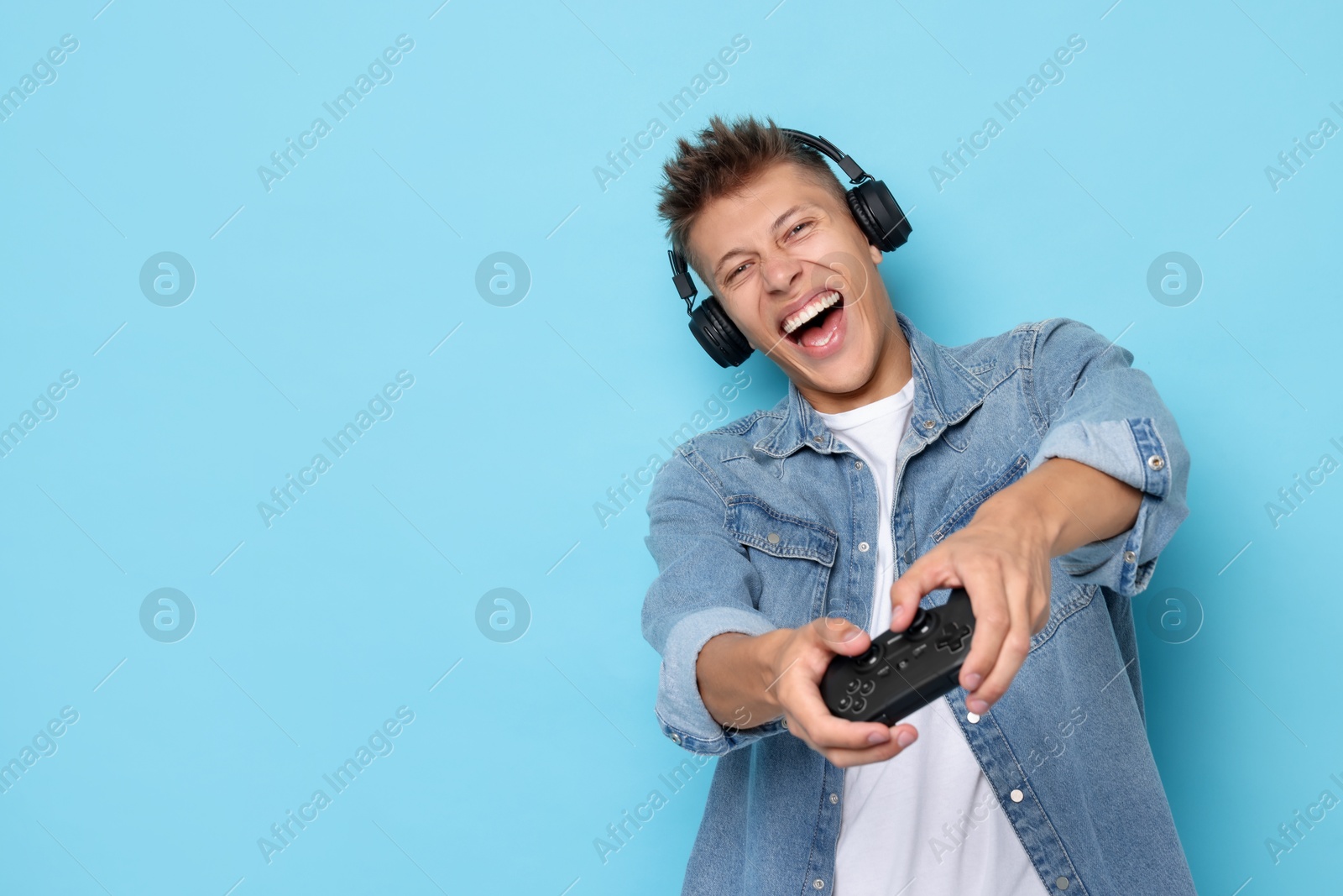 Photo of Happy young man playing video games with controller on light blue background, space for text