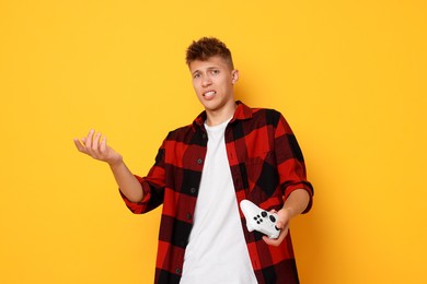 Photo of Unhappy young man with controller on orange background