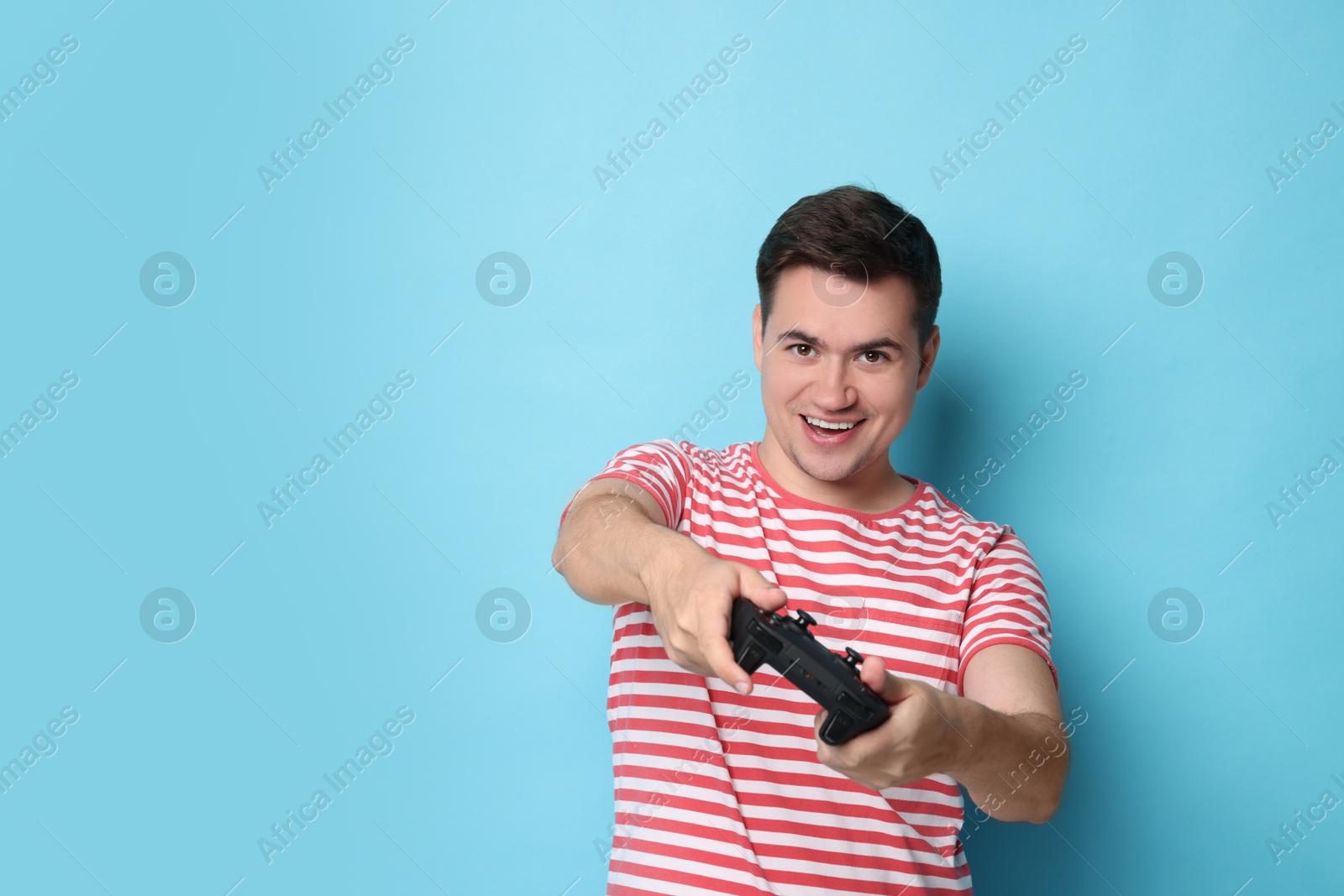 Photo of Happy young man playing video games with controller on light blue background, space for text