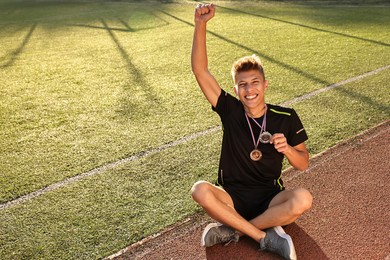 Photo of Happy winner with different medals sitting at stadium on sunny day. Space for text