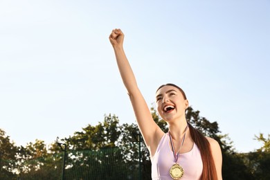 Happy winner with golden medal outdoors, low angle view. Space for text