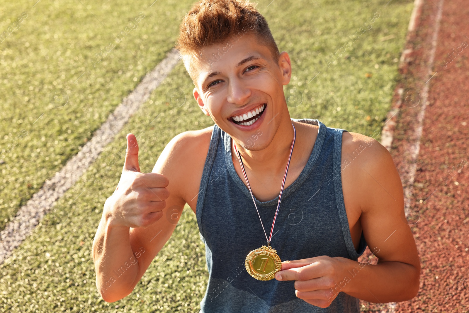 Photo of Happy winner with golden medal showing thumbs up at stadium on sunny day