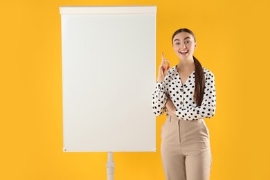 Photo of Happy woman near flip chart on orange background. Mockup for design