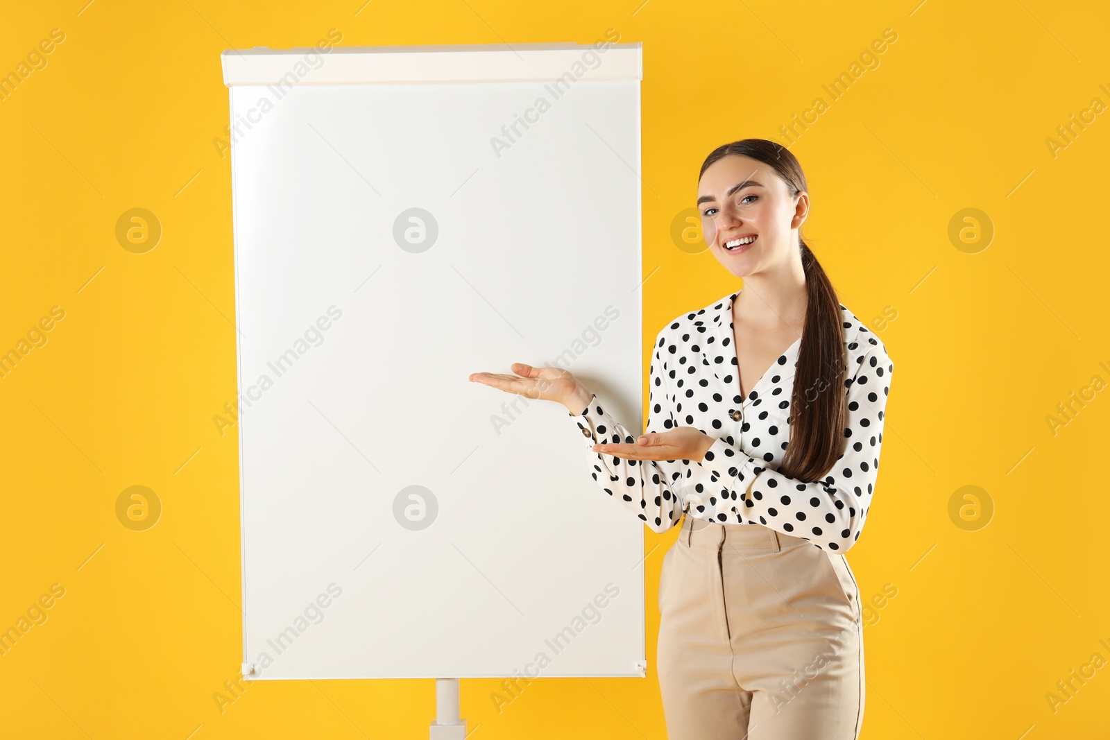 Photo of Happy woman near flip chart on orange background. Mockup for design