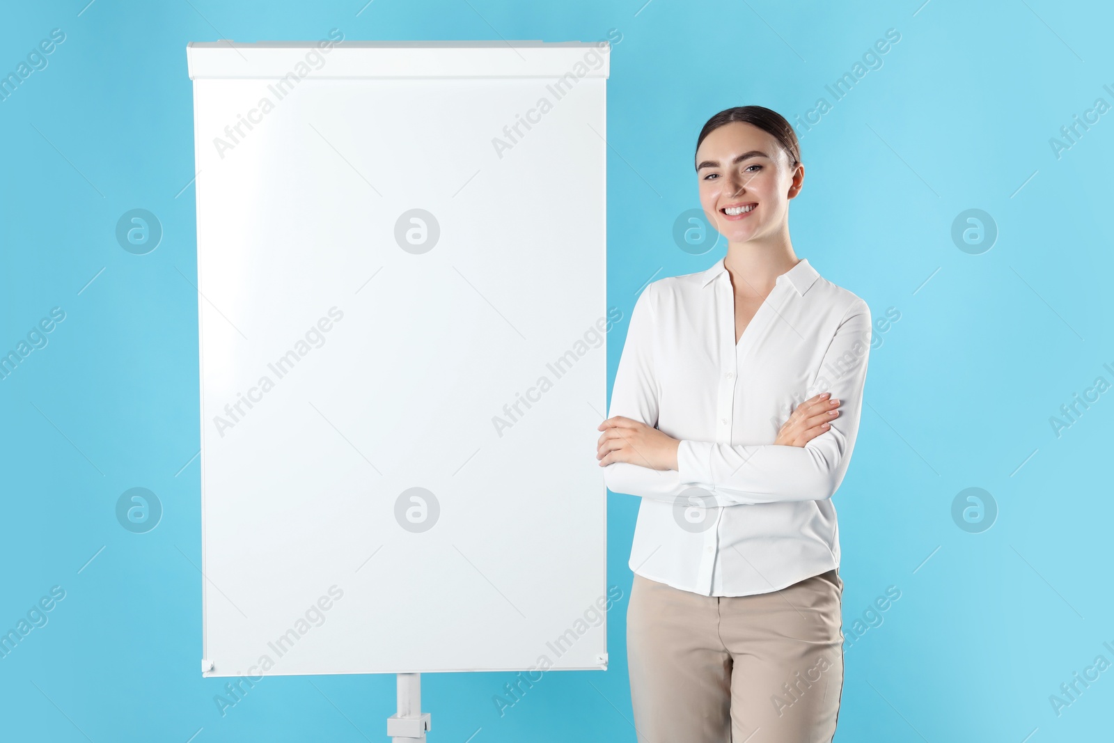 Photo of Happy woman near flip chart on light blue background. Mockup for design