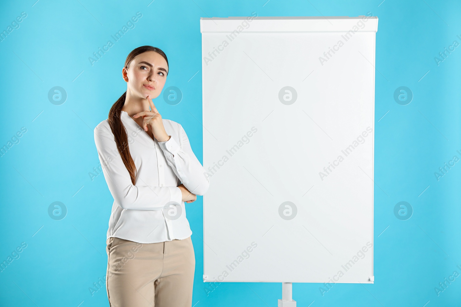 Photo of Thoughtful woman near flip chart on light blue background. Mockup for design