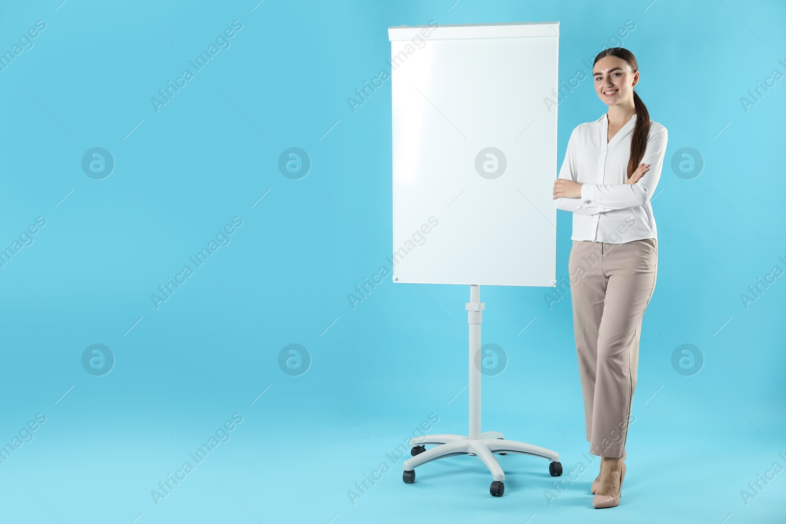 Photo of Happy woman near flip chart on light blue background. Mockup for design