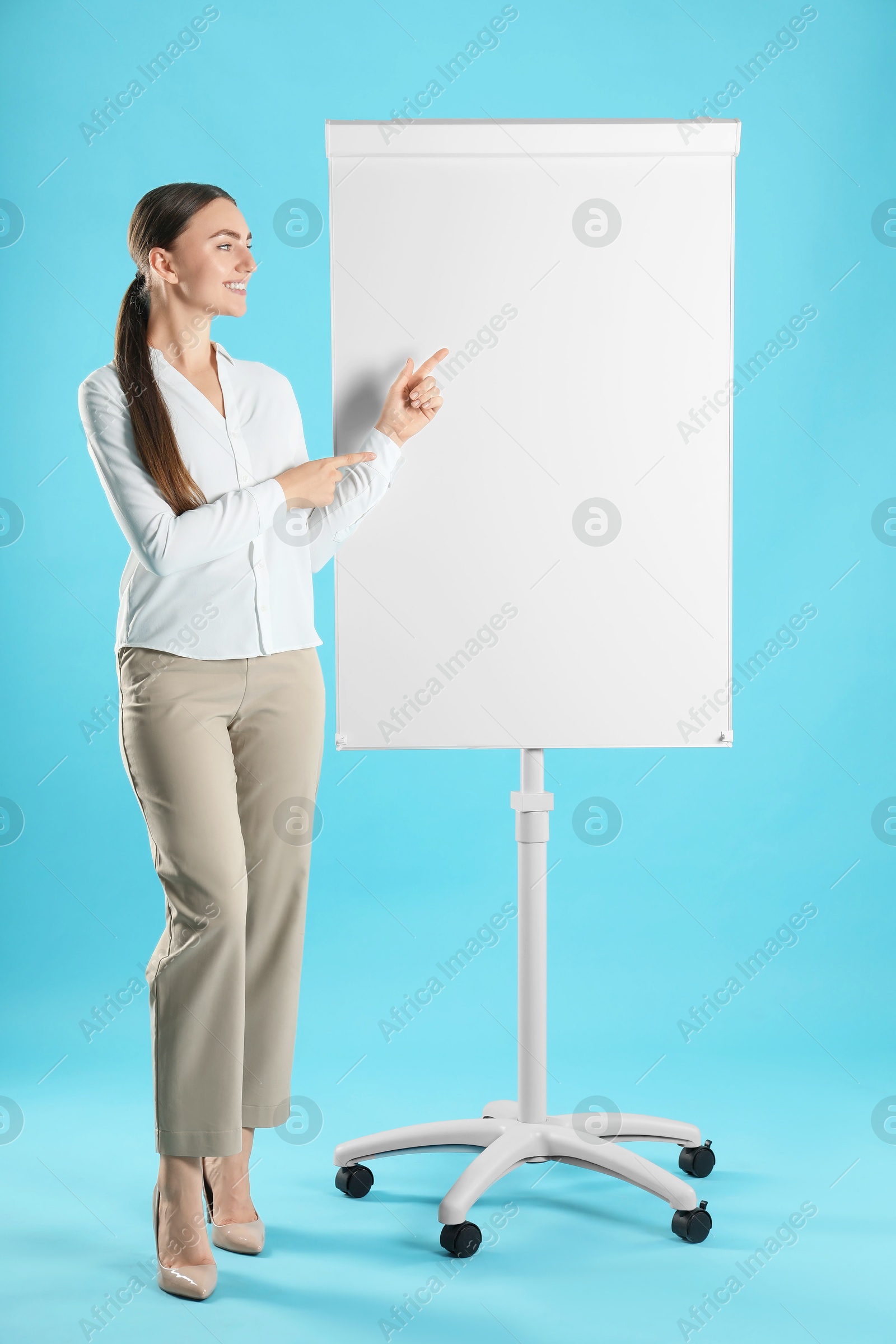 Photo of Happy woman near flip chart on light blue background. Mockup for design