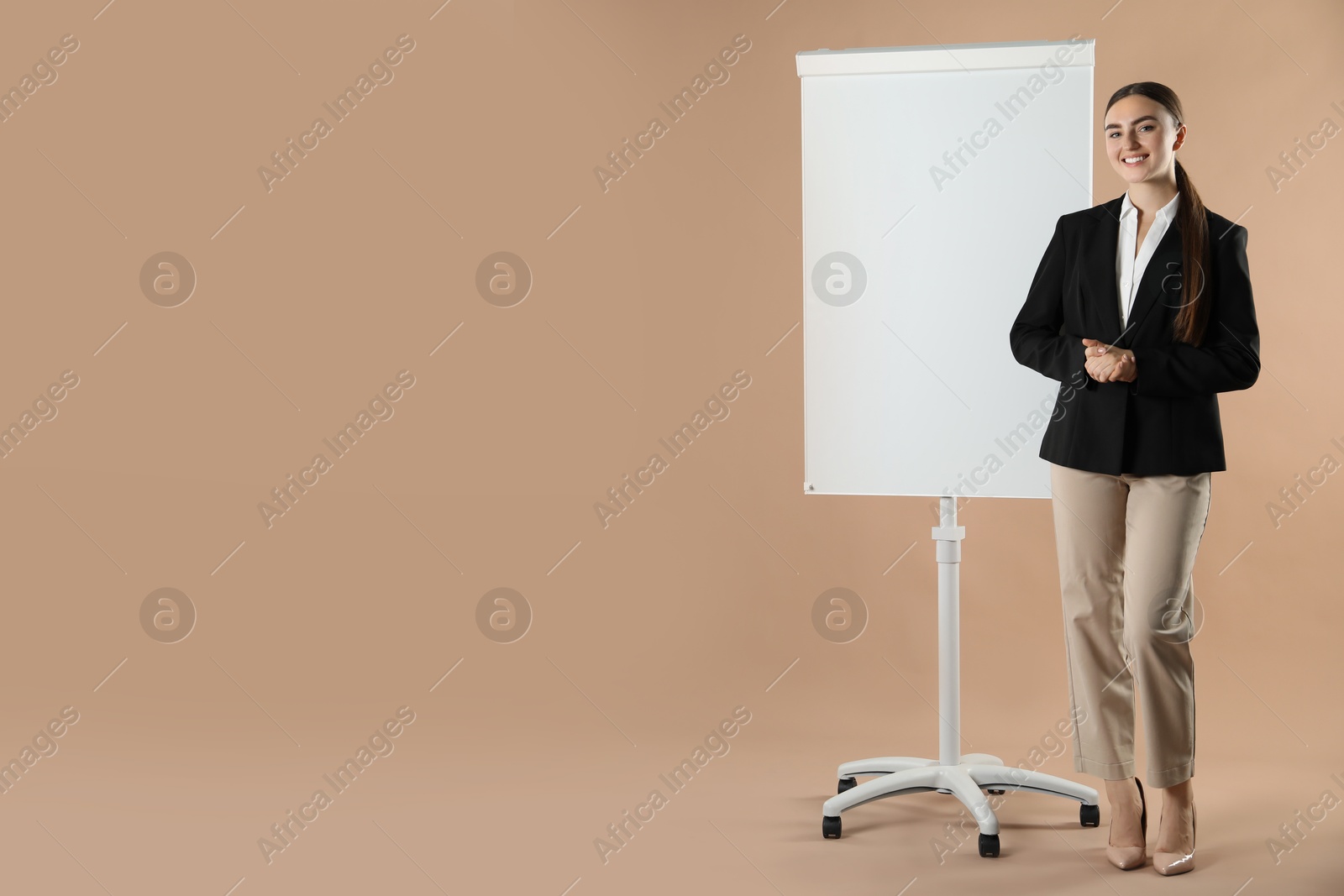 Photo of Happy woman near flip chart on pale brown background. Mockup for design