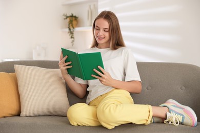 Teenage girl reading book on sofa at home