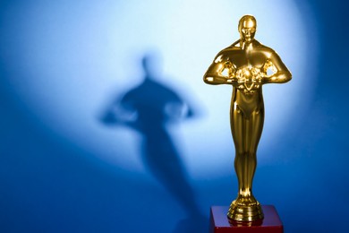 Photo of Golden trophy in shape of human figure on blue background, space for text