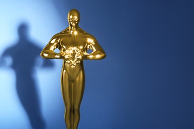 Photo of Golden trophy in shape of human figure on blue background, closeup. Space for text