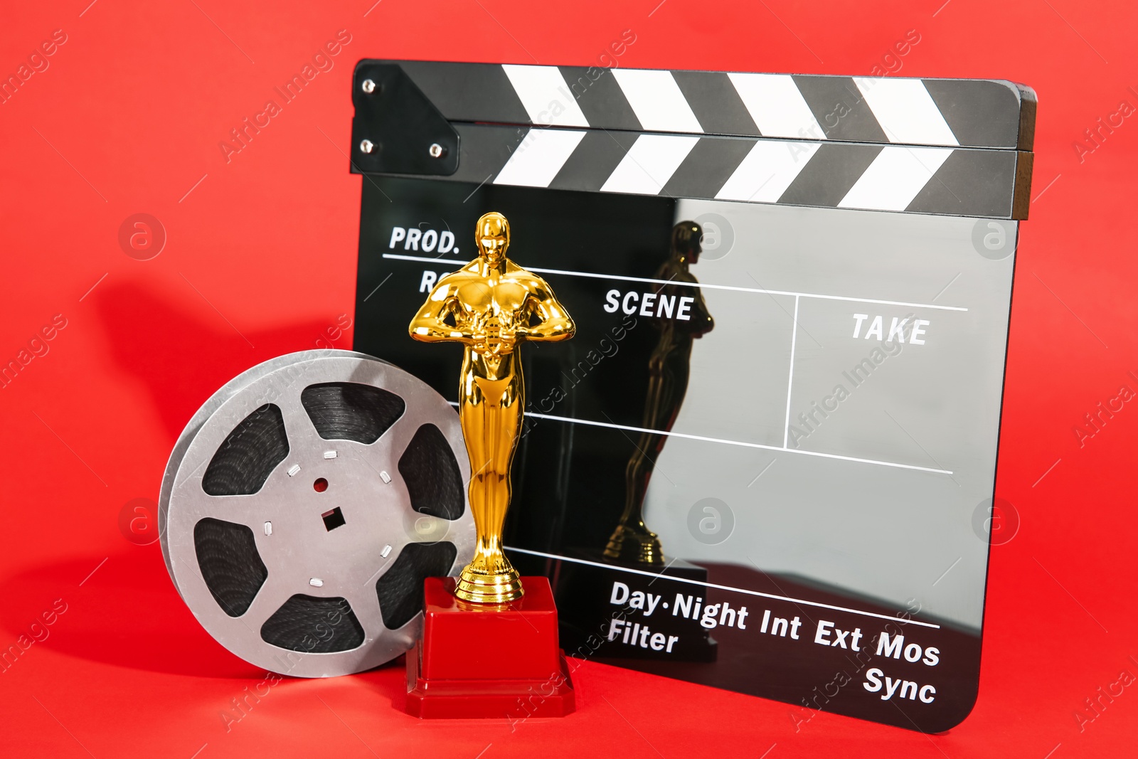 Photo of Golden trophy in shape of human figure, movie clapper and film reel on red background