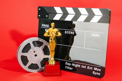 Photo of Golden trophy in shape of human figure, movie clapper and film reel on red background