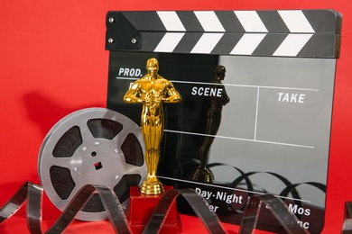 Photo of Golden trophy in shape of human figure, movie clapper and film reel on red background