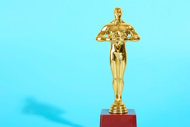 Golden trophy in shape of human figure on light blue background, space for text