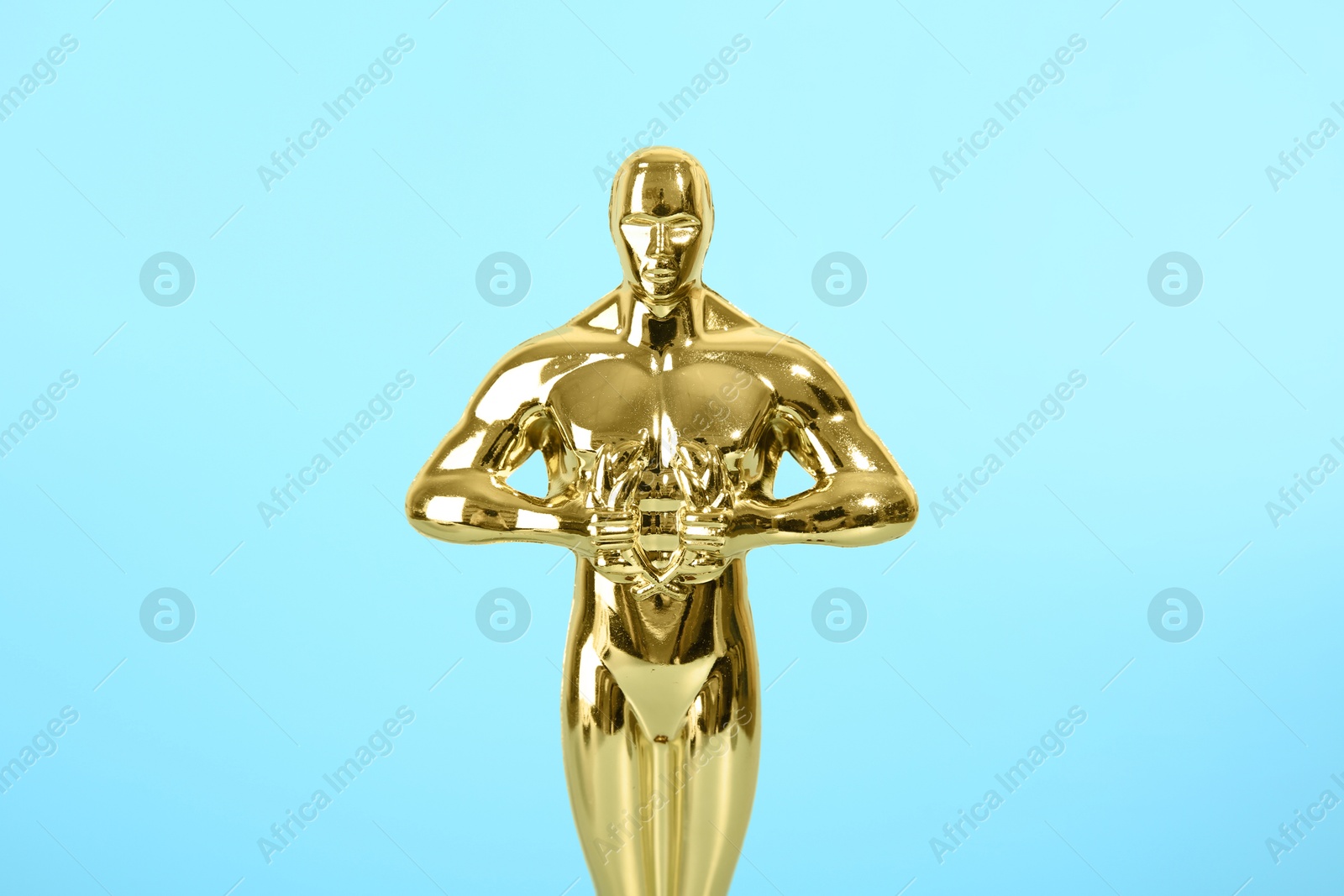 Photo of Golden trophy in shape of human figure on light blue background, closeup