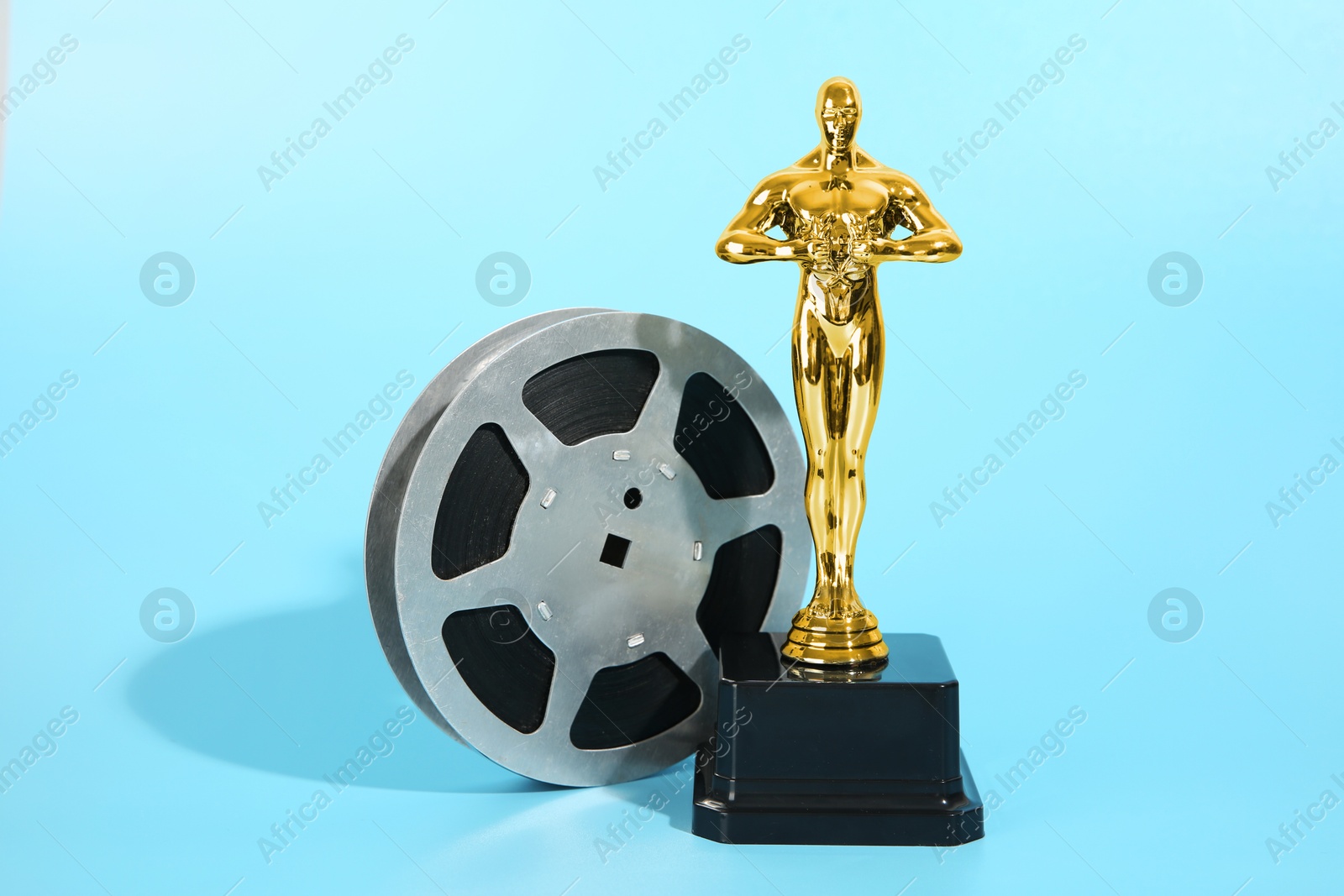 Photo of Golden trophy in shape of human figure and film reel on light blue background