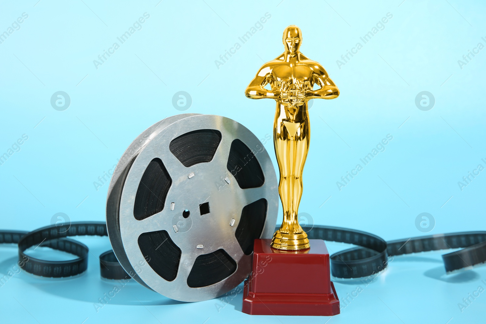 Photo of Golden trophy in shape of human figure and film reel on light blue background