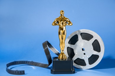 Photo of Golden trophy in shape of human figure and film reel on light blue background