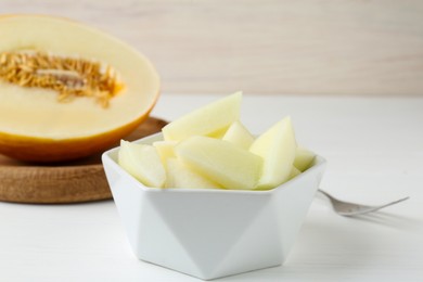 Photo of Cut tasty melon in bowl on white table, closeup