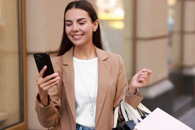 Photo of Happy woman with shopping bags using smartphone outdoors