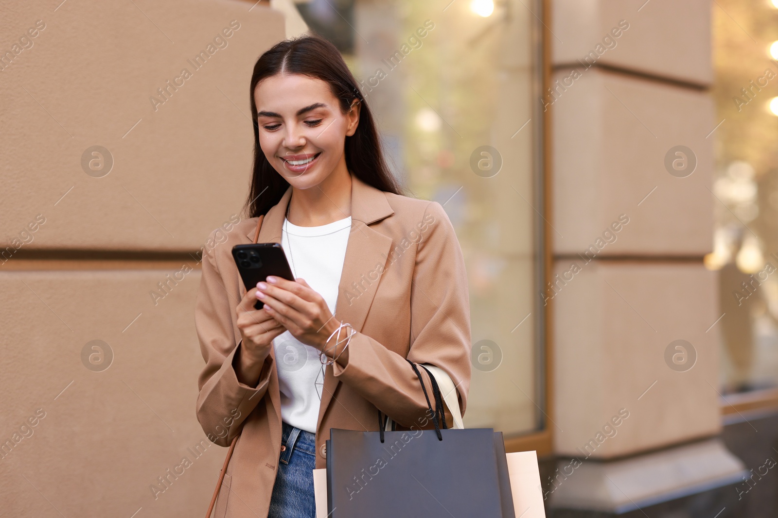 Photo of Happy woman with shopping bags using smartphone outdoors