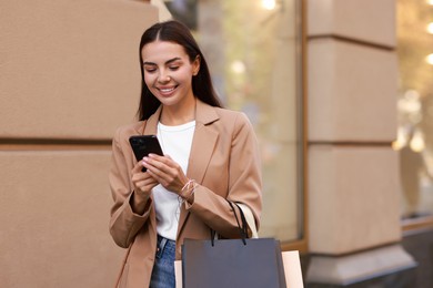 Photo of Happy woman with shopping bags using smartphone outdoors