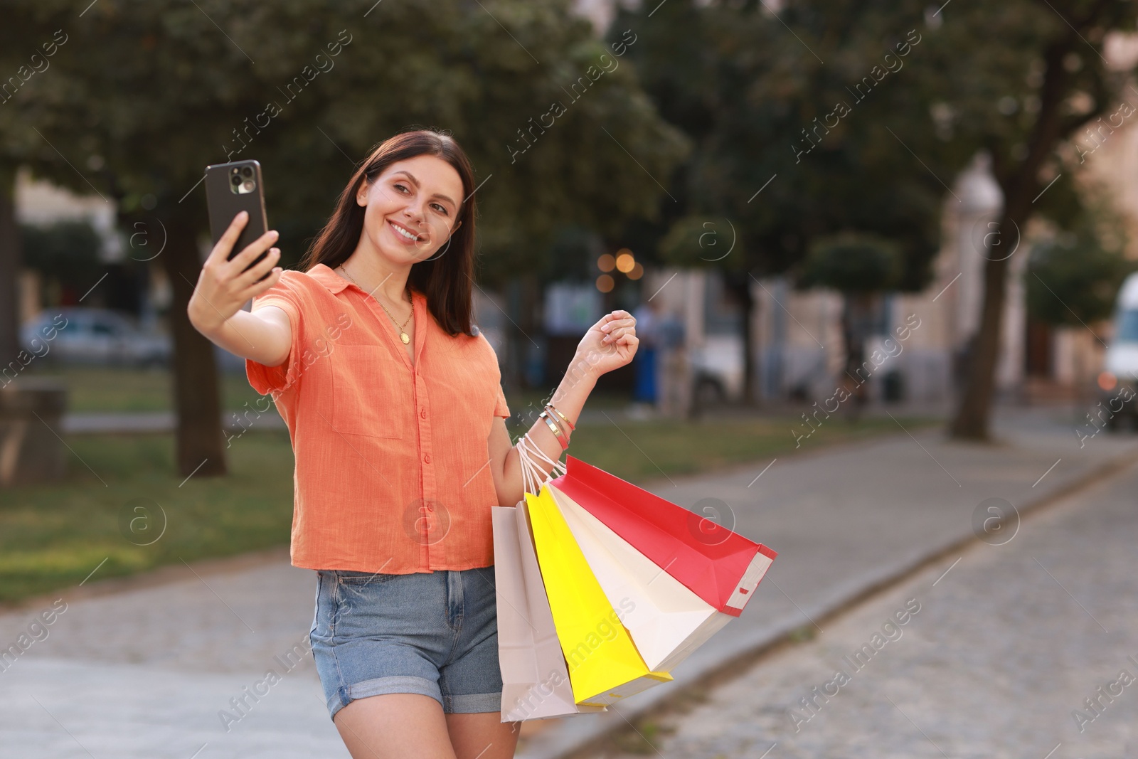 Photo of Happy woman with colorful shopping bags taking selfie outdoors