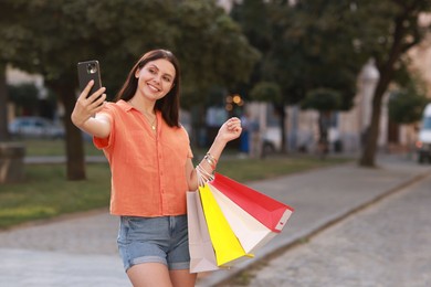 Photo of Happy woman with colorful shopping bags taking selfie outdoors