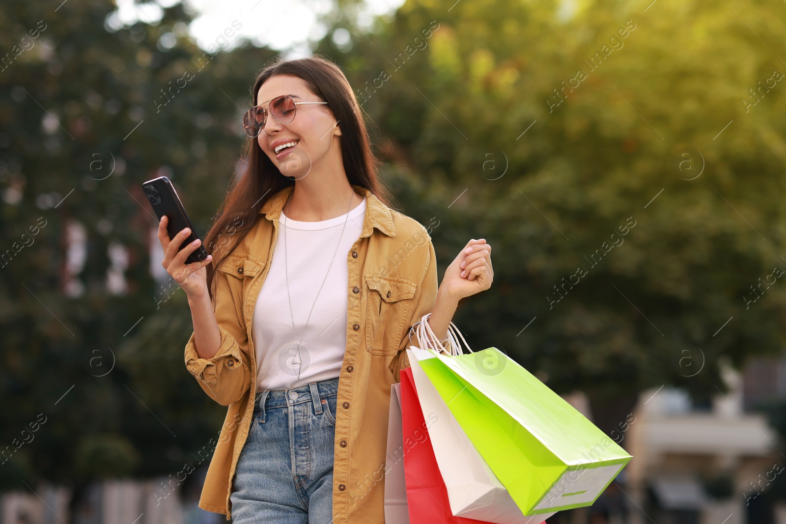 Photo of Happy woman with colorful shopping bags using smartphone outdoors