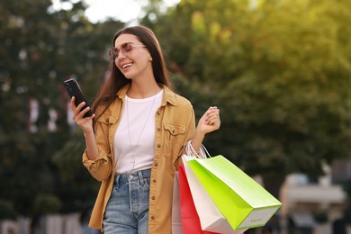 Photo of Happy woman with colorful shopping bags using smartphone outdoors