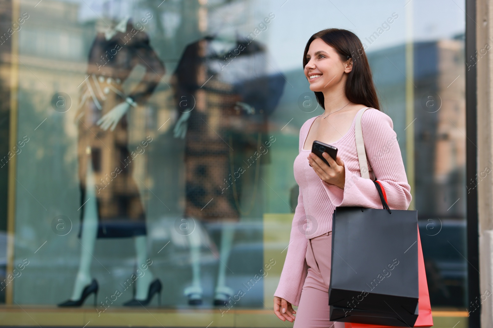 Photo of Happy woman with colorful shopping bags using smartphone outdoors, space for text